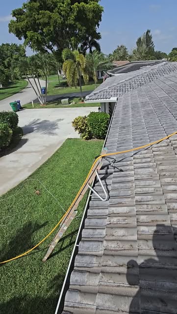 Soft washing a tile roof, hose running along the tiles on a clear day.